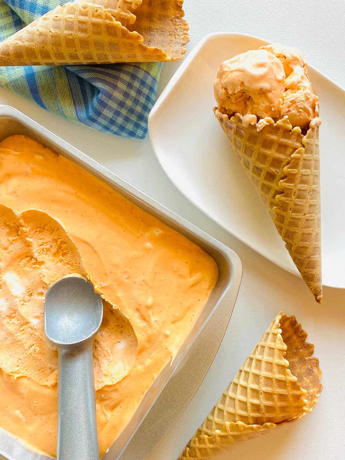 Container filled with Thai ice cream with scoop and ice cream cones surrounding it.