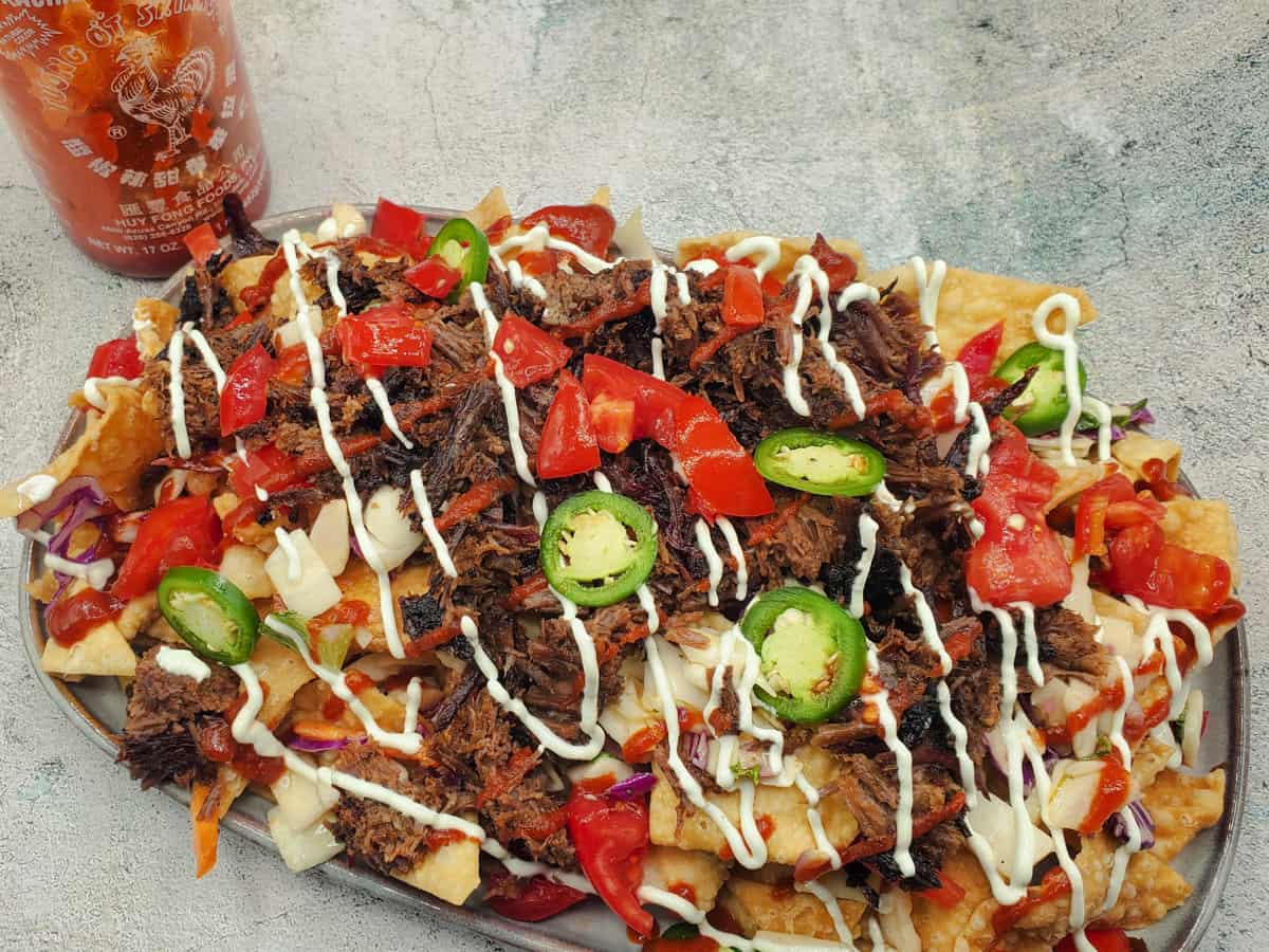 Up close of Asian beef short rib nachos piled high with toppings.