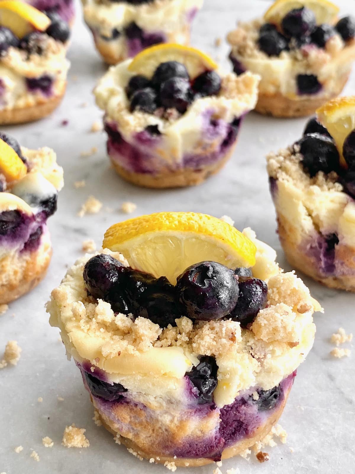 Blueberry cheesecake cupcakes on light colored surfaces.