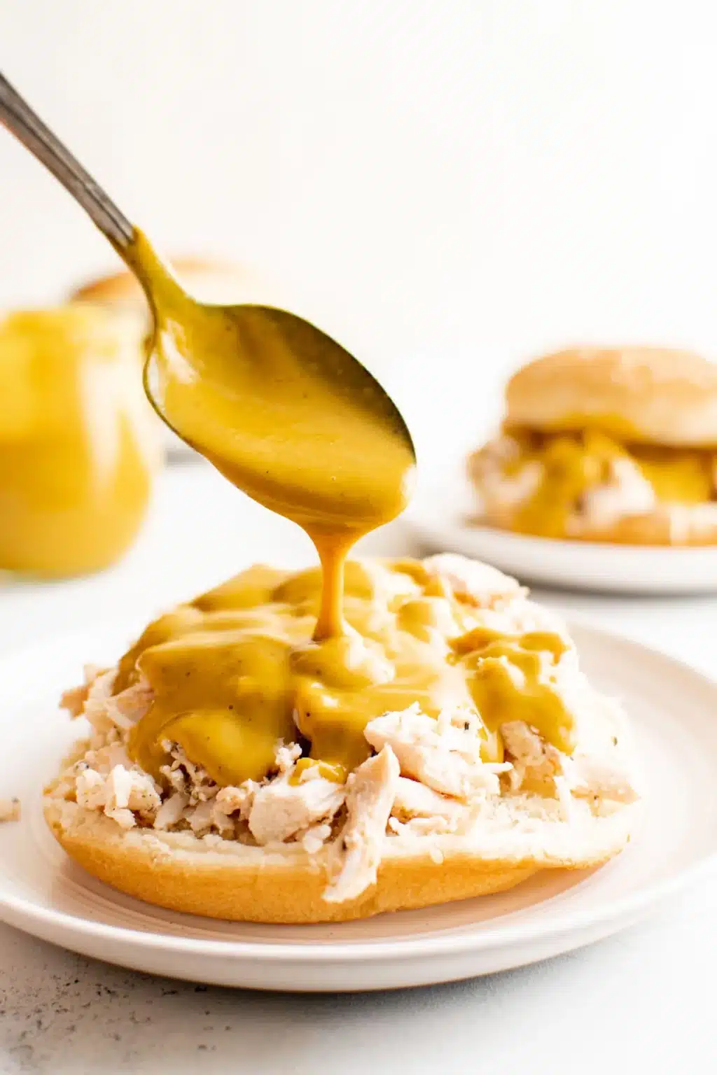 Spoon drizzling Carolina gold bbq sauce on chicken sandwich.