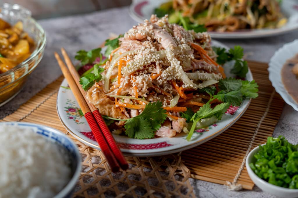 Chinese cold shredded chicken salad on a decorative plate with chopsticks.