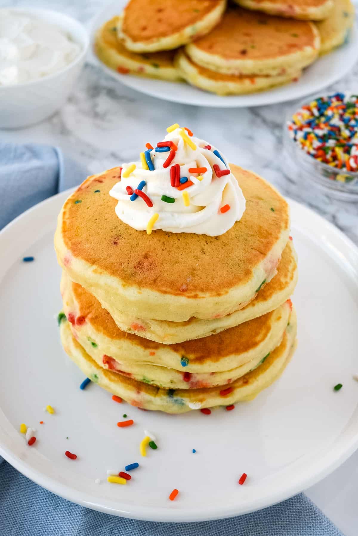 Stack of sprinkle filled pancakes on a white plate.