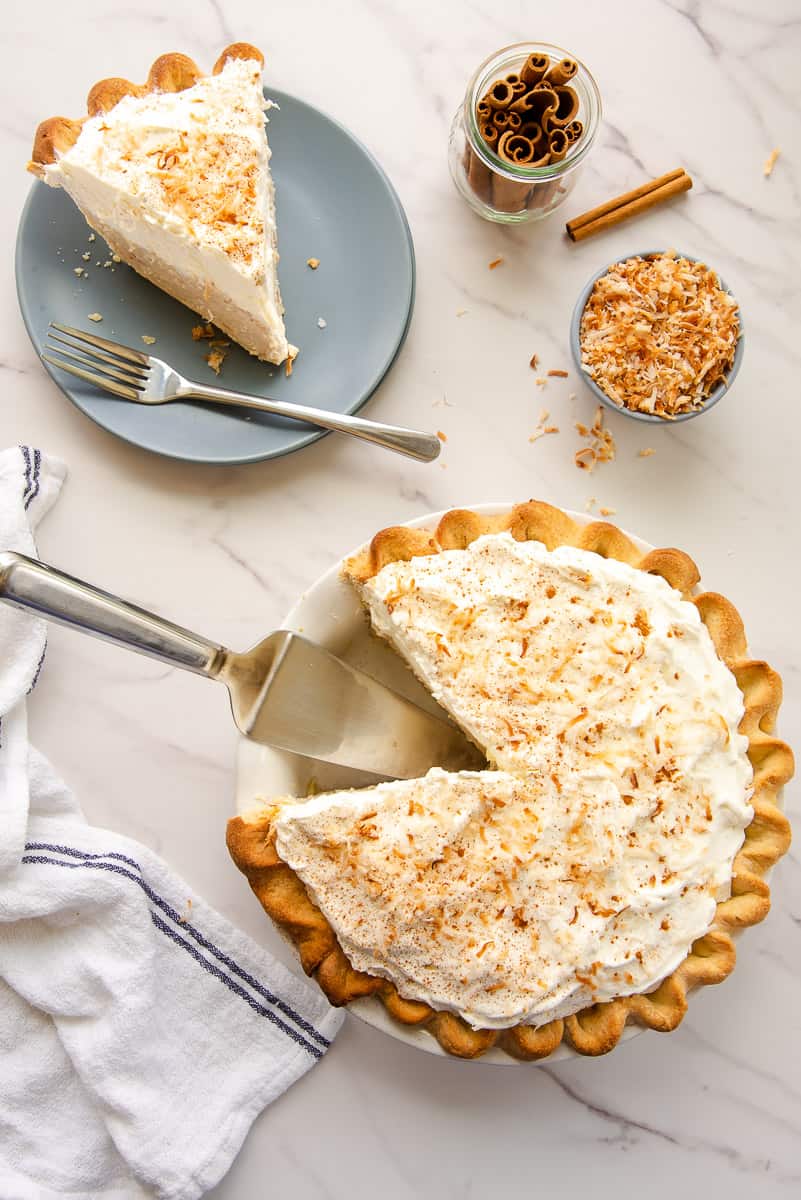 Slice of coconut rum cream pie on a blue plate with more in the background.