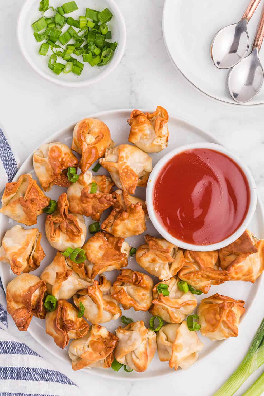 Crab rangoon on a white plate with a dipping sauce.