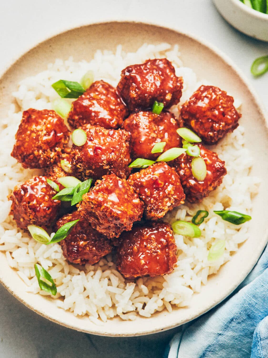 Breaded tofu nuggets with sweet chili on white rice on a plate.