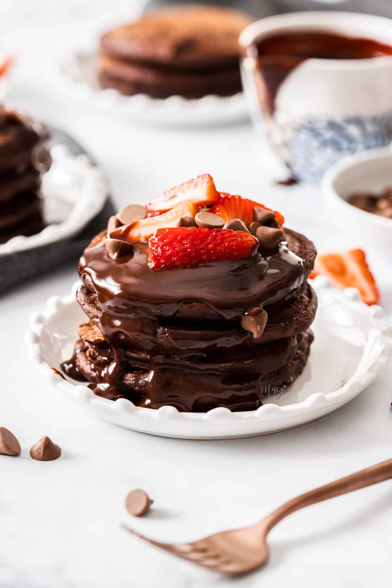 Stack of double chocolate pancakes with chocolate syrup, chocolate chips, and sliced strawberries.