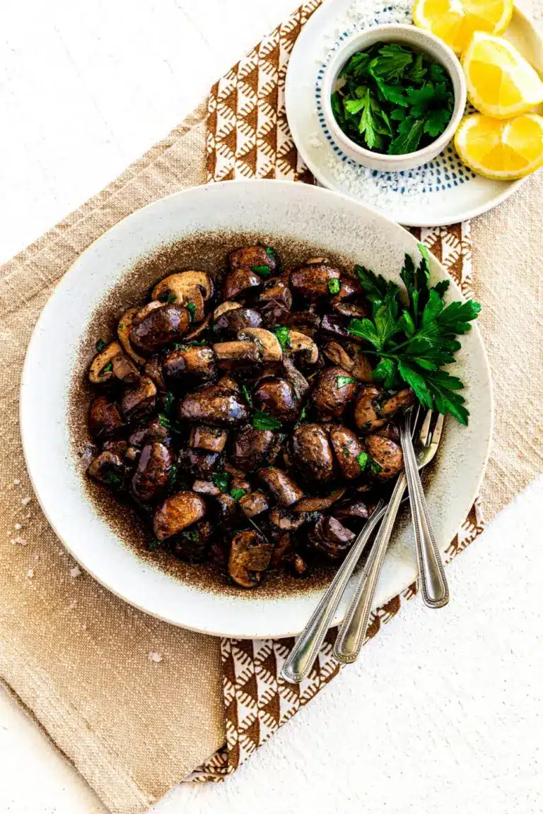 Sauteed mushrooms on a white plate with herb and lemon in the background.