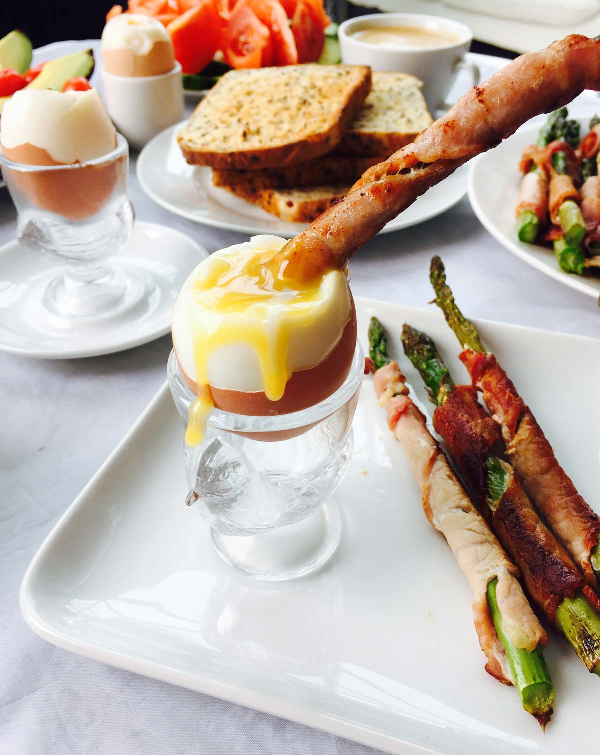 Bacon wrapped asparagus with runny boiled egg on a square plate.