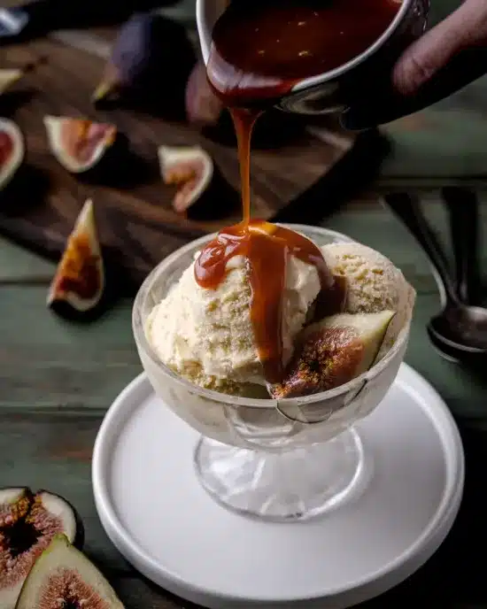 Hand pouring sauce on fig ice cream.