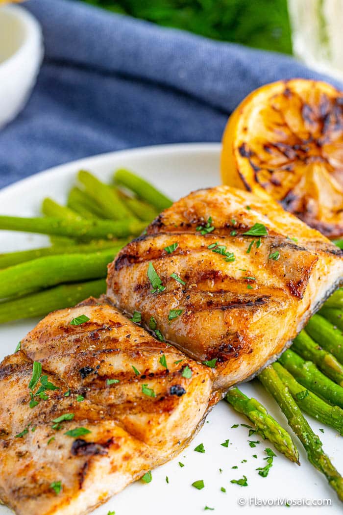 Grilled mahi mahi fillet with asparagus on a white plate.