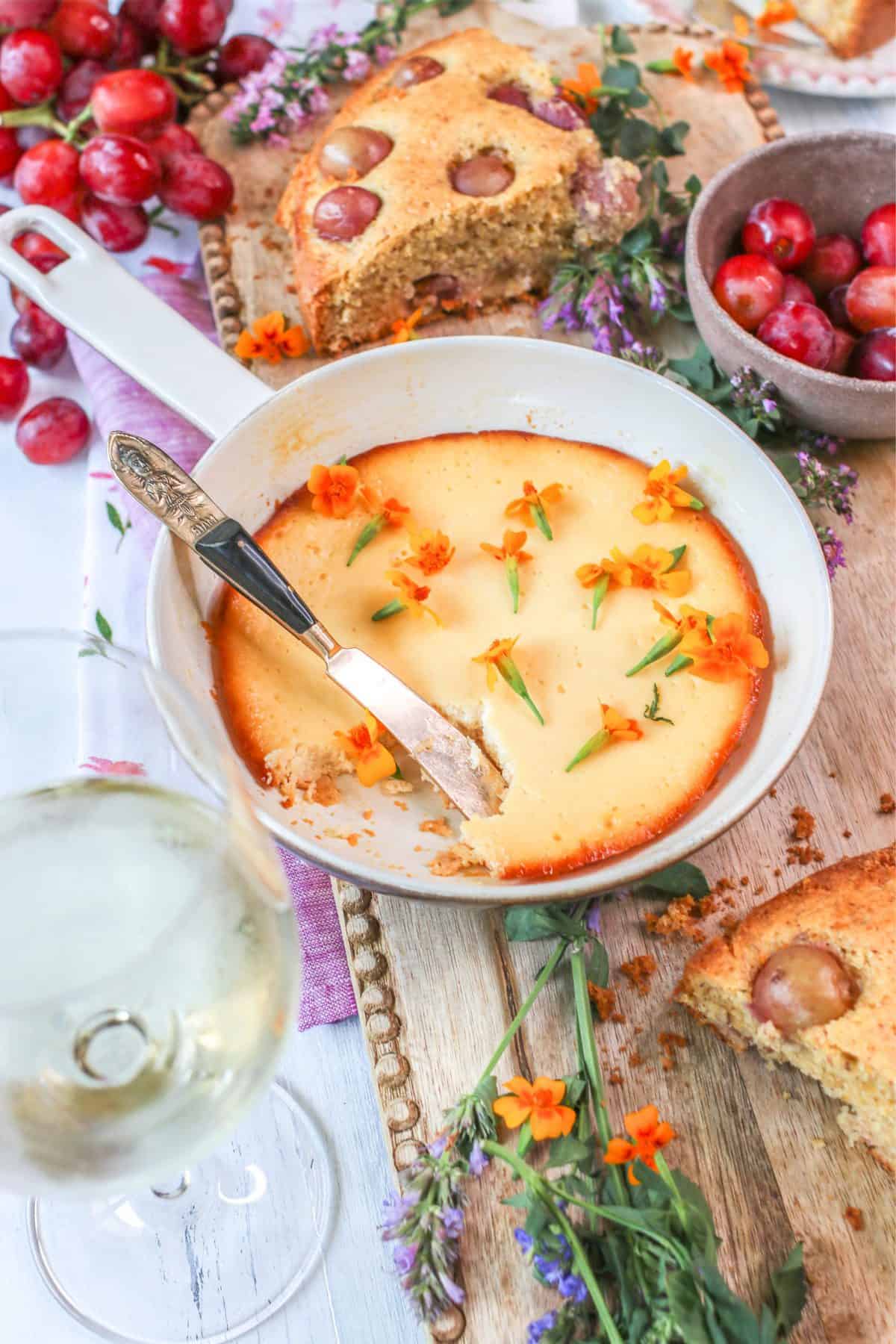 Baked sweet ricotta with orange zest dessert in a pan with various ingredients and flowers surrounding it.