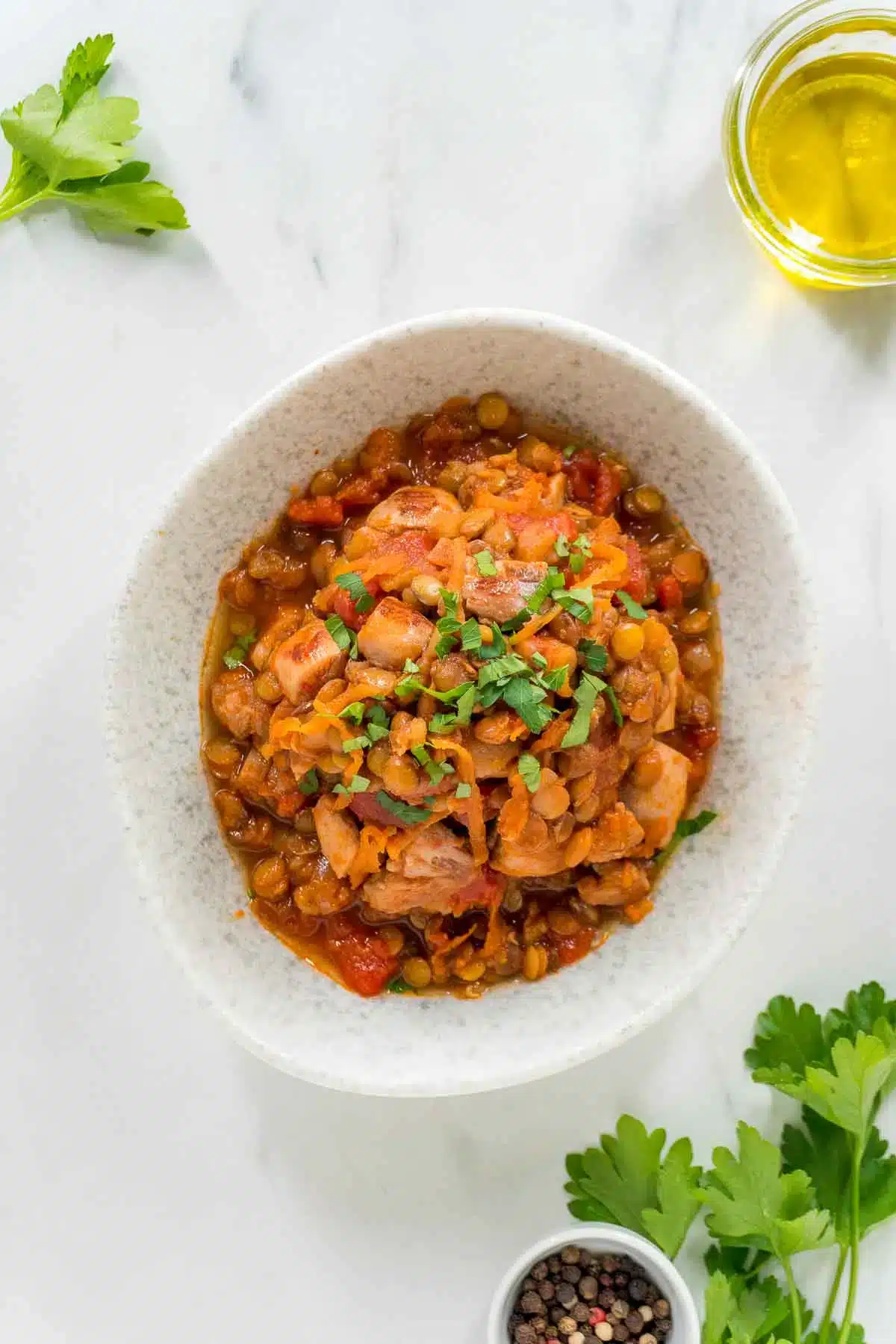 Harissa chicken and lentils in a white bowl with herbs and peppercorn in the background.