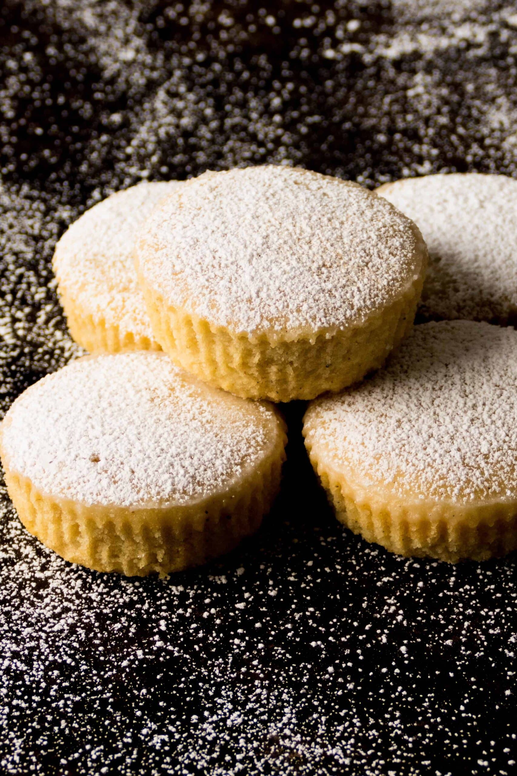 Stack of flat cupcakes with powdered sugar on a dark surface.