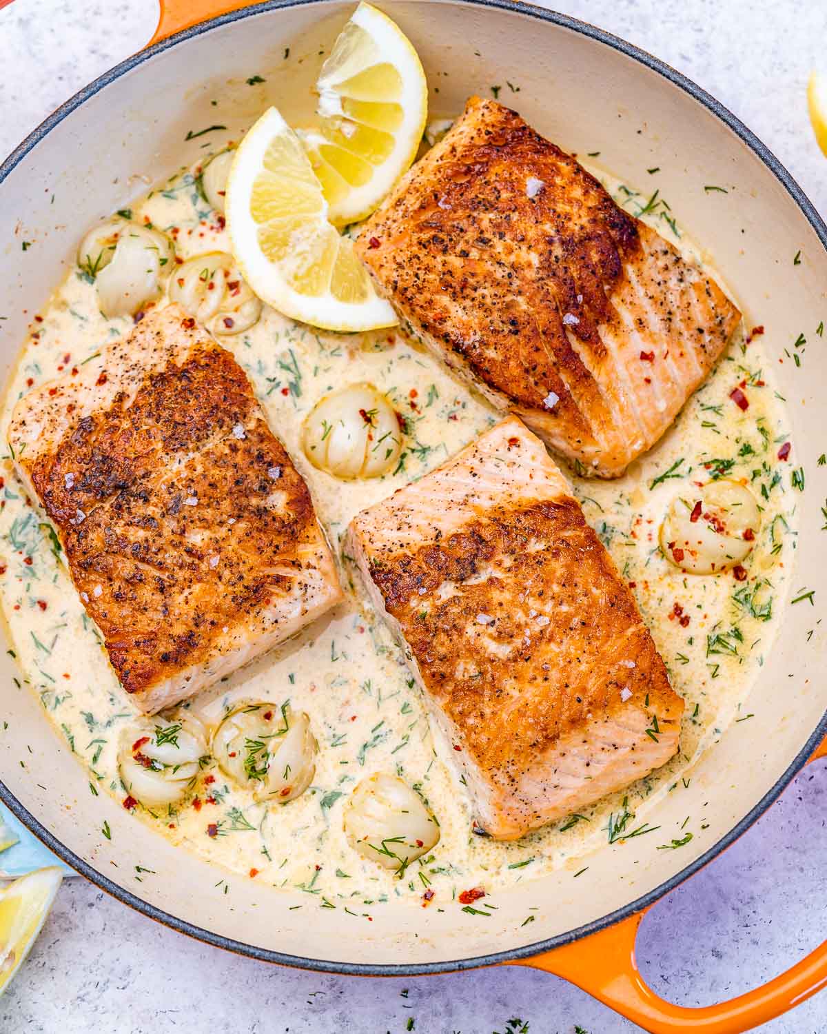 Seared salmon with sauce in a pan with garlic and lemon.