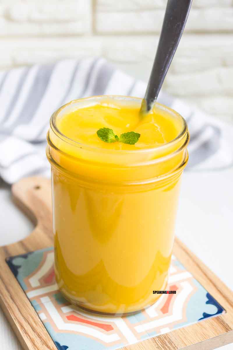 Jar filled with orange mango sauce with a sprig of mint and a spoon.