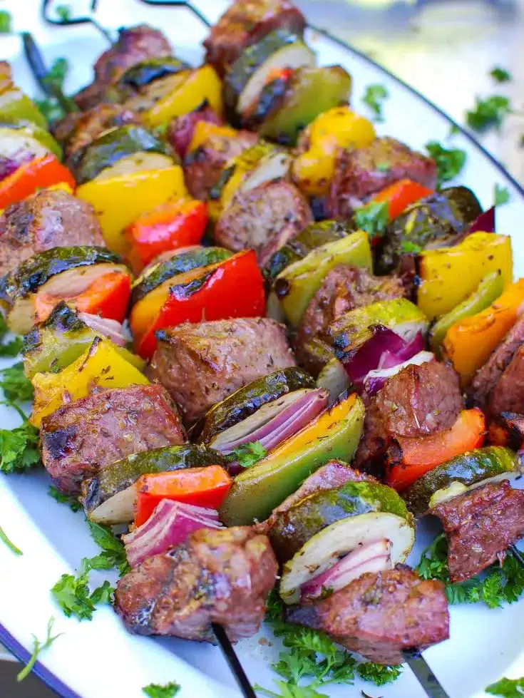 Beef and colorful vegetables on skewers on a white plate.