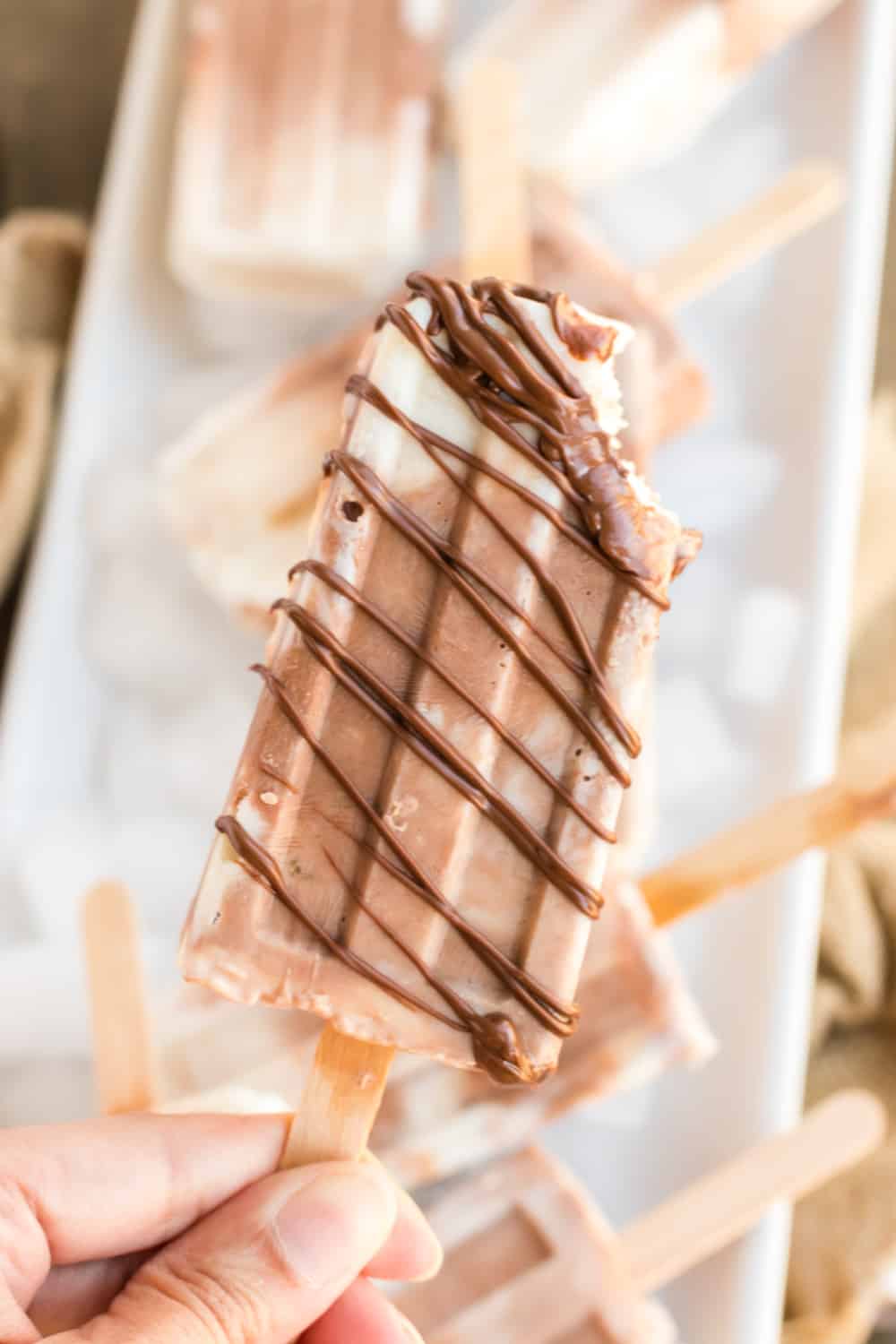 Hand holding banana Nutella popsicle with a drizzle of Nutella.