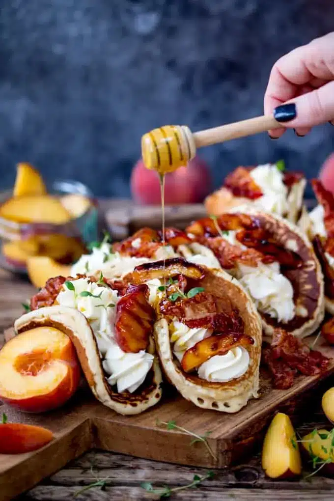 Hand drizzling honey over pancake tacos with caramelized peaches and pancetta.