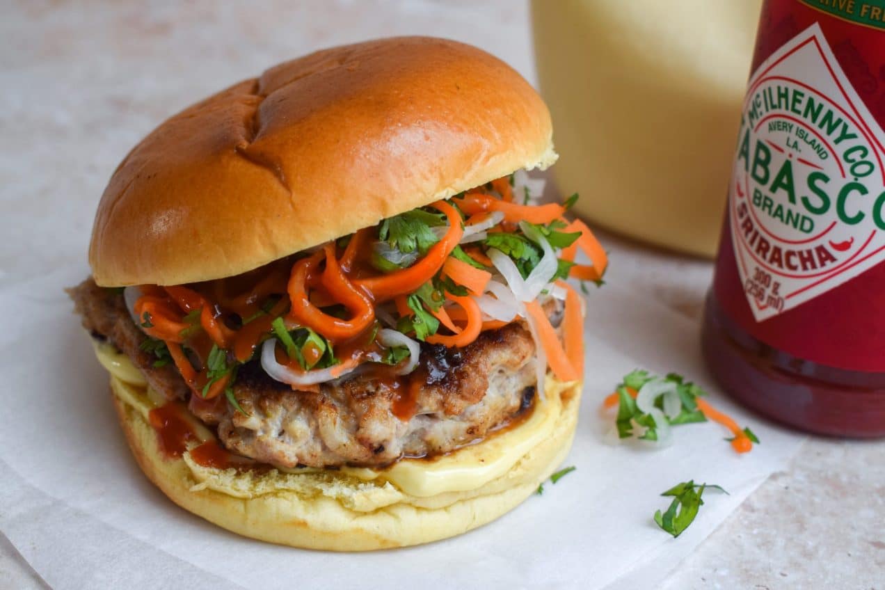 Pork banh mi burger with shredded carrot, daikon, and mayo on a bun.