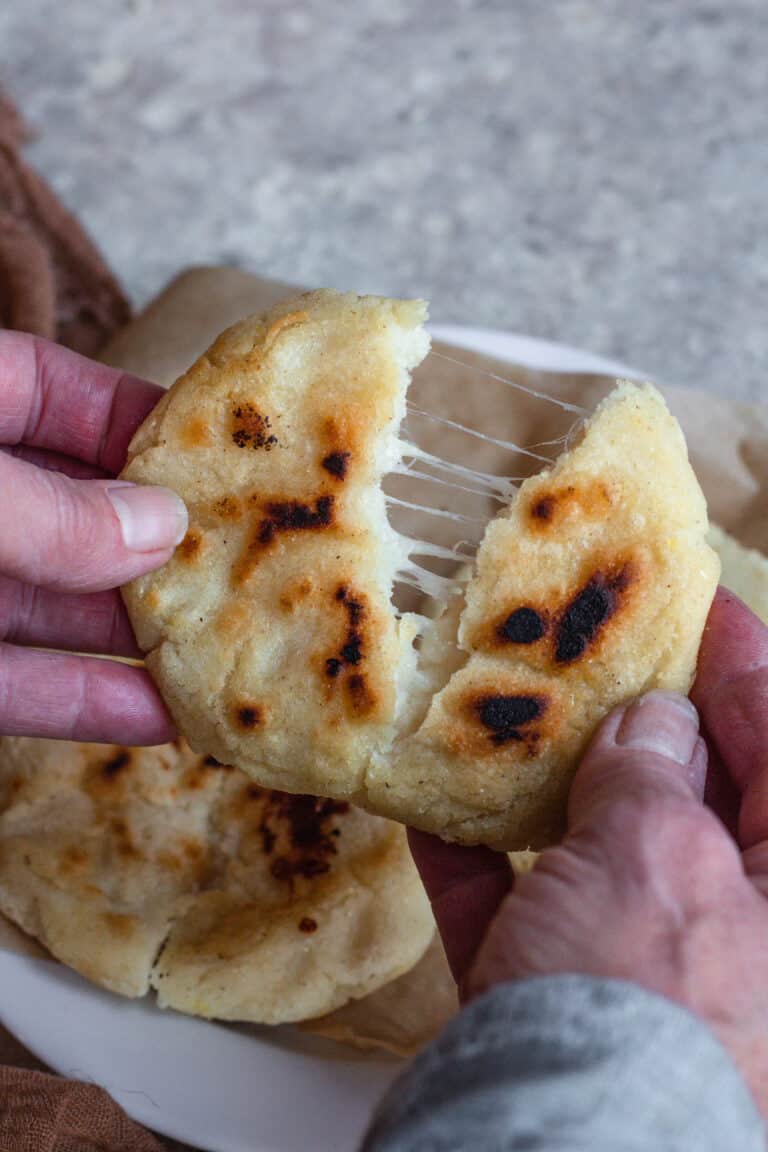 Hand holding pupusas torn apart with cheese pull.