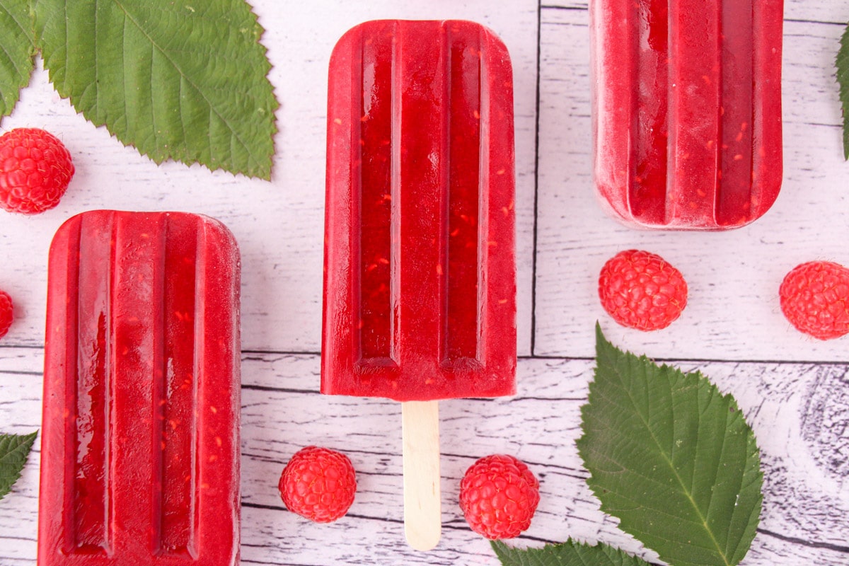 Raspberry popsicles with raspberries on a white surface.