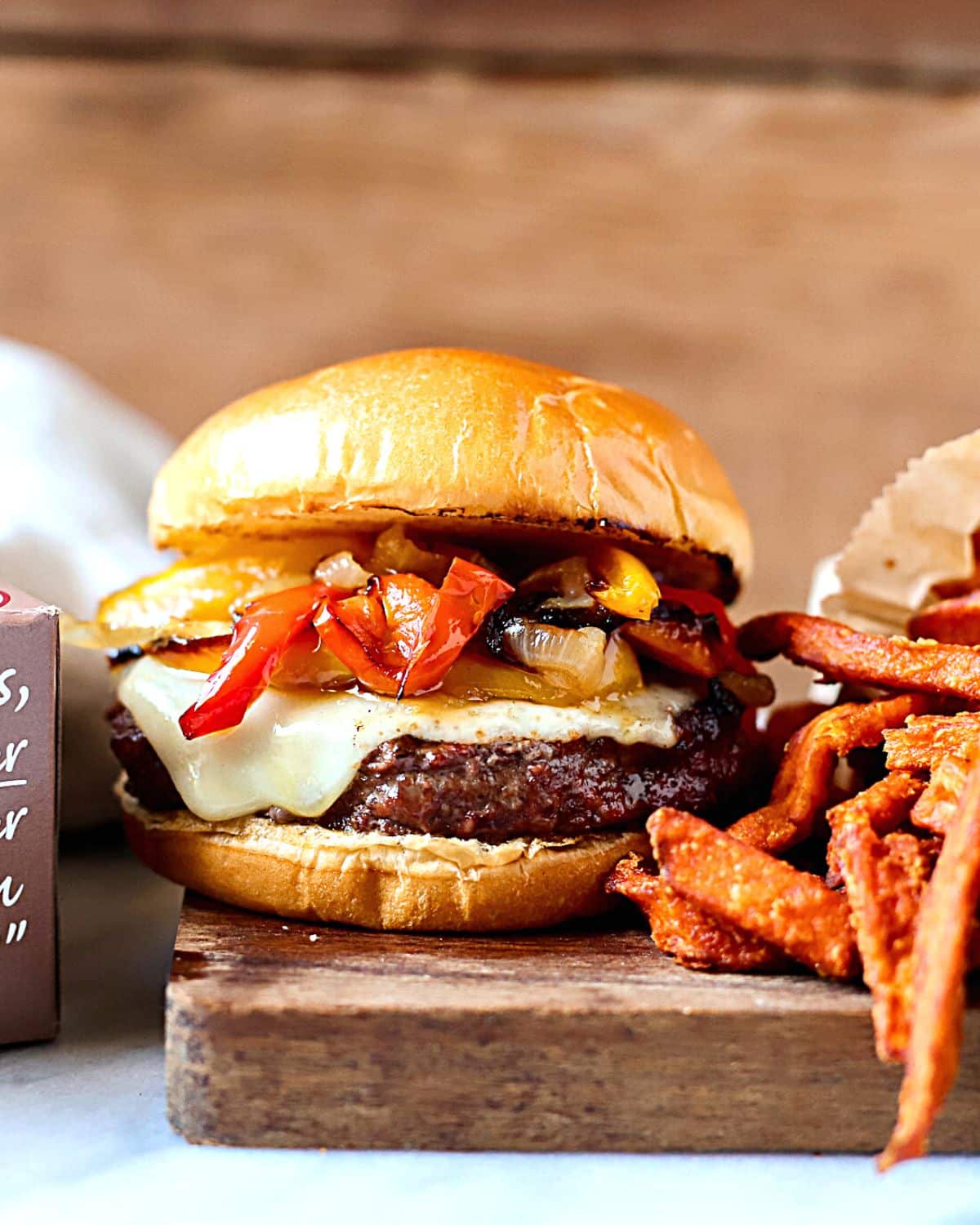 Philly cheesesteak burger on a bun with sweet potato fries.