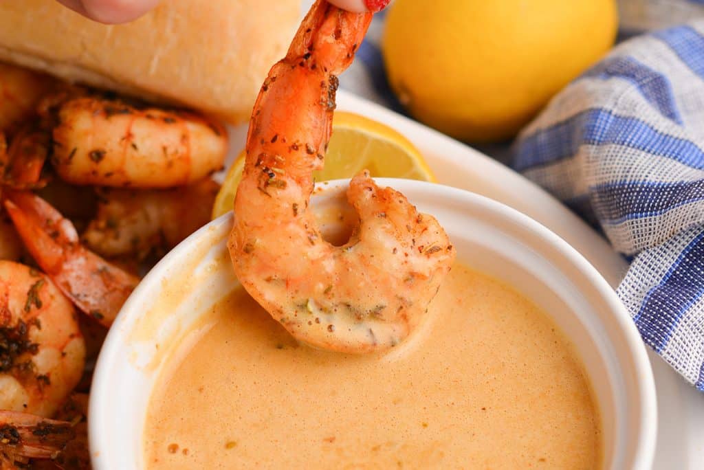Hand dipping shrimp into seafood sauce.