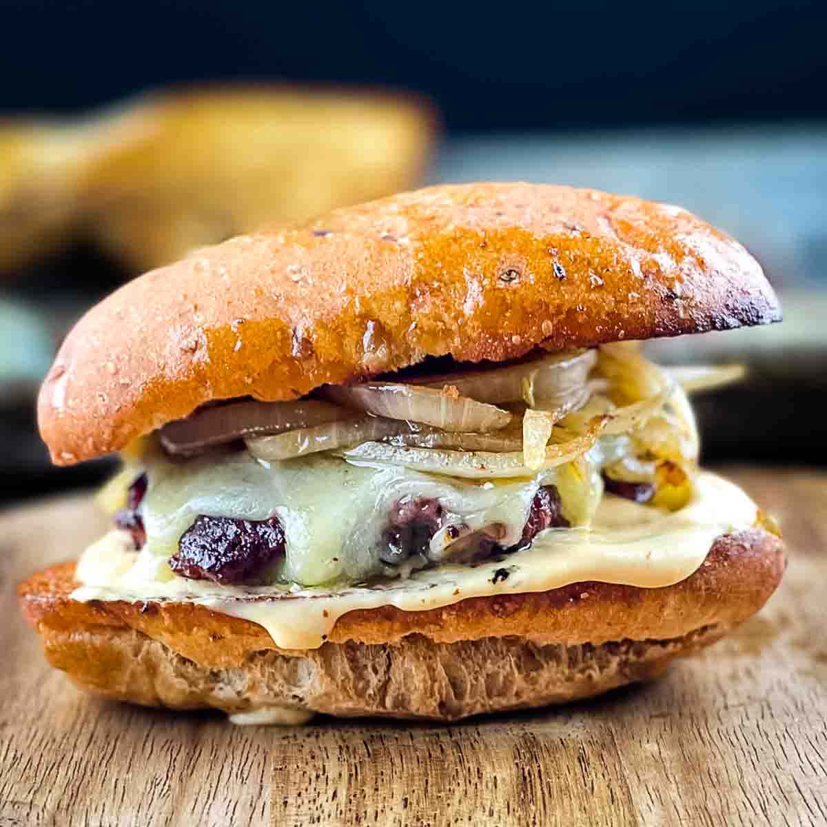 Smashburger with caramelized onions and cheese on a bun on a wooden surface.