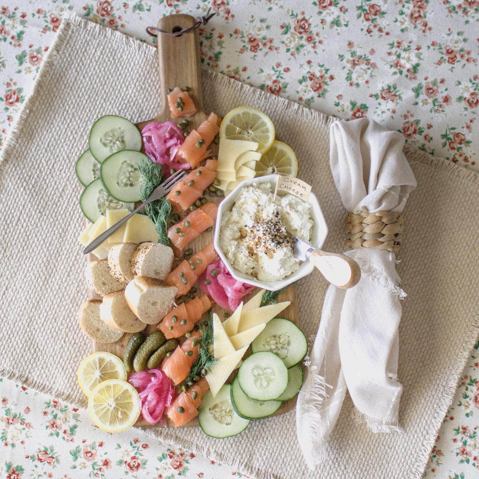 Smoked salmon charcuterie board with various foods like pickles, sliced cucumbers, pickled onions, cheese, etc.