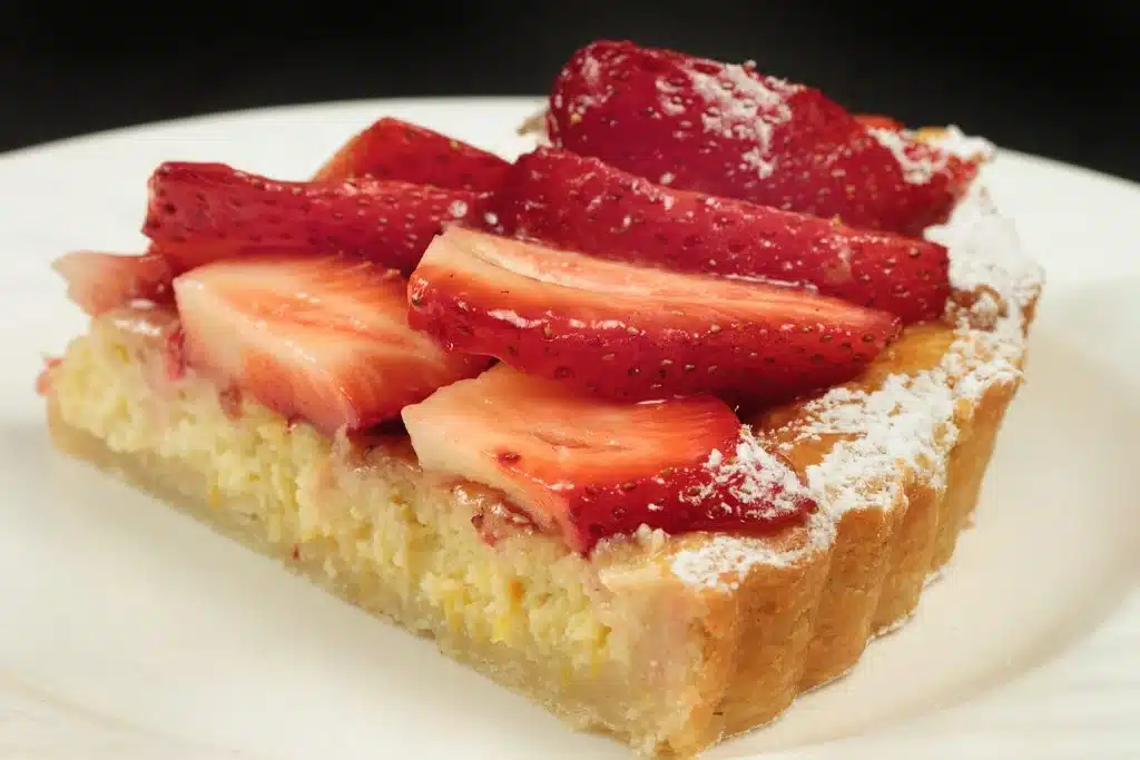 Slice of strawberry tart on a white plate with a dark background.