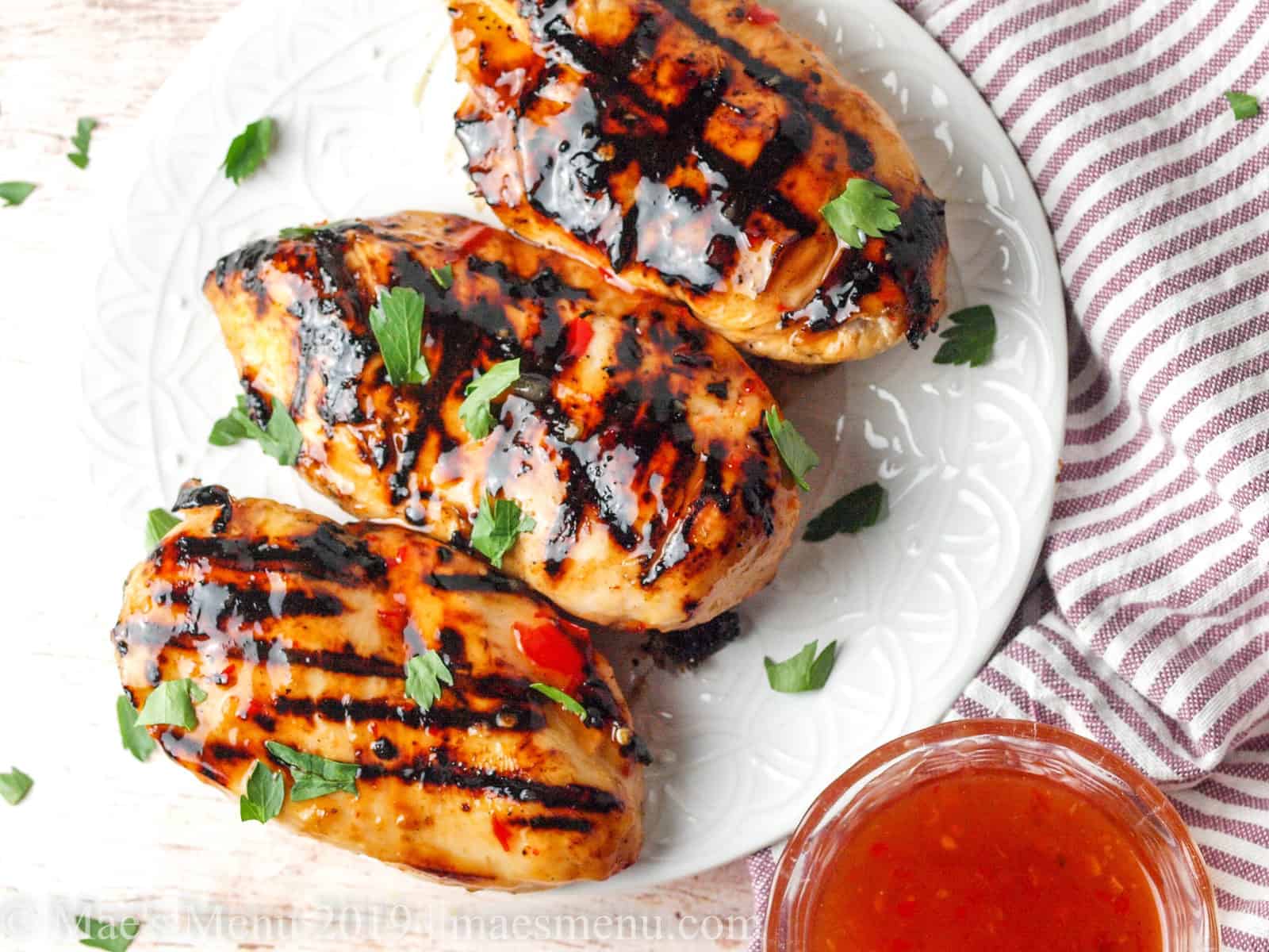 Sweet chili lime chicken on a white plate with more dipping sauce on the side.