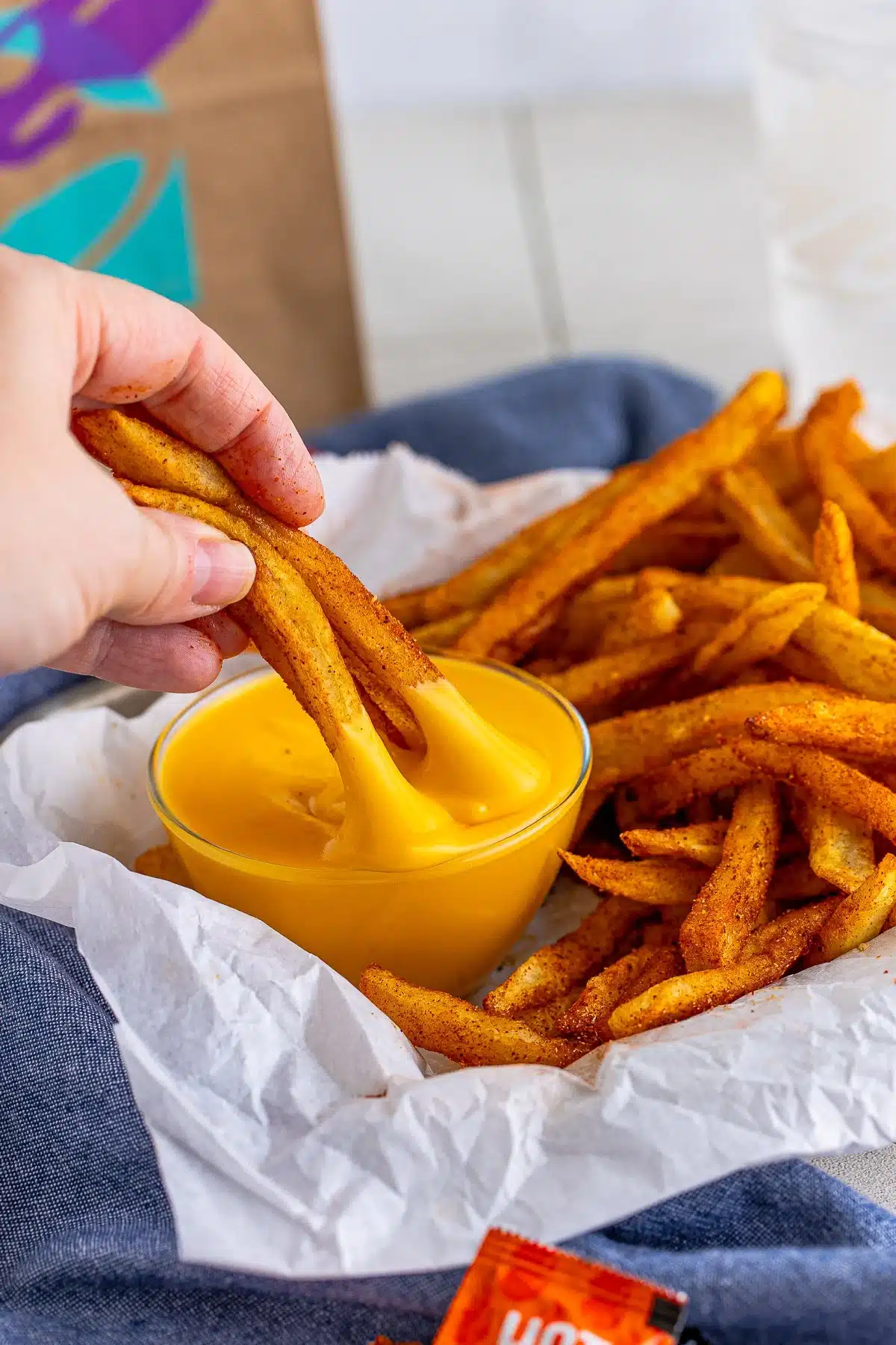 Hand dipping seasoned fries into cheese sauce.