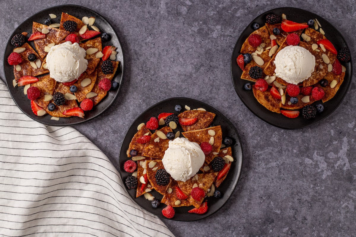 Three small black plates full of mixed berry nachos.