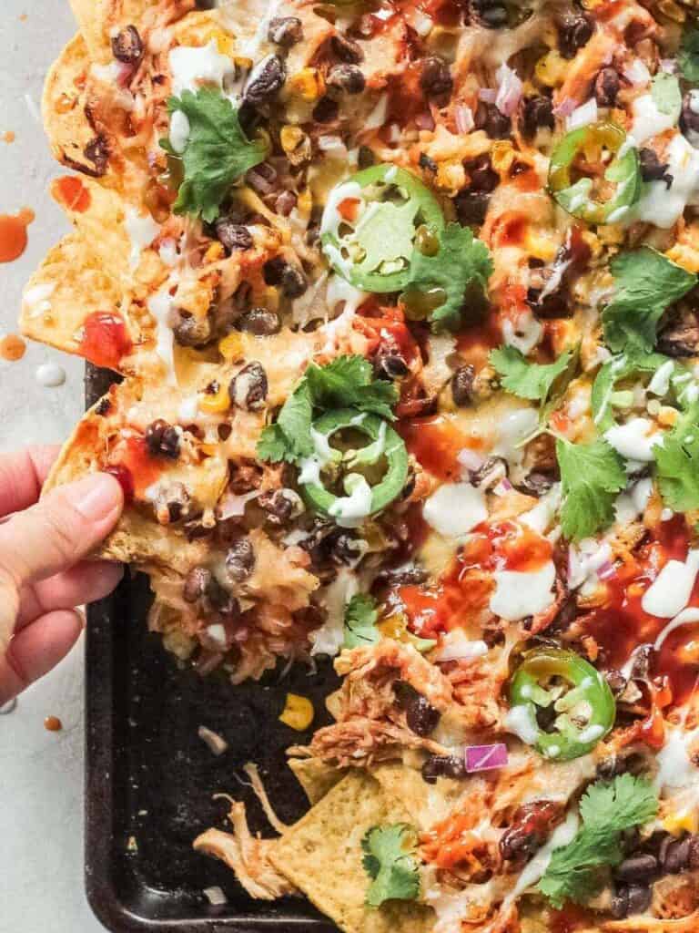 Hand picking up bbq chicken nachos.