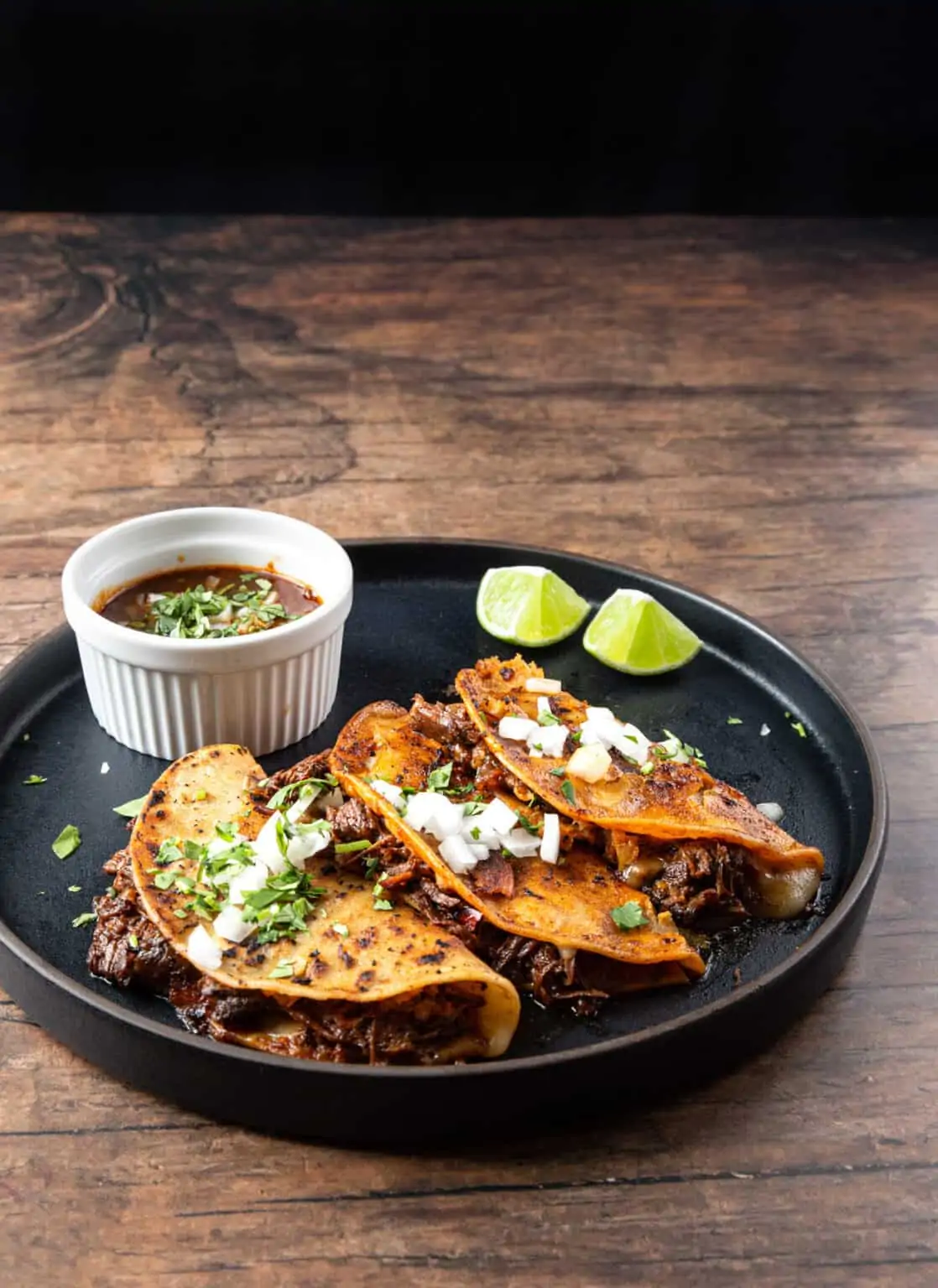 Birria tacos on a dark plate.