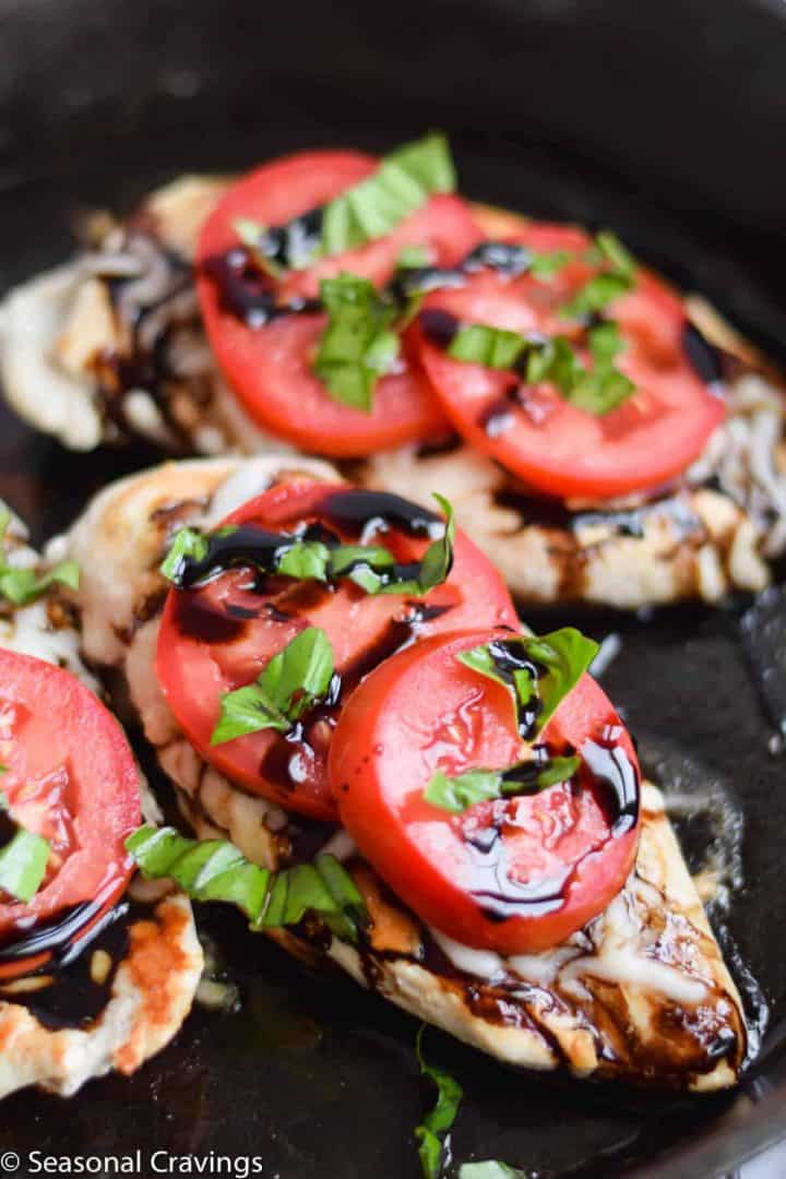 Caprese chicken with tomato, basil, and balsamic glaze on a dark surface.