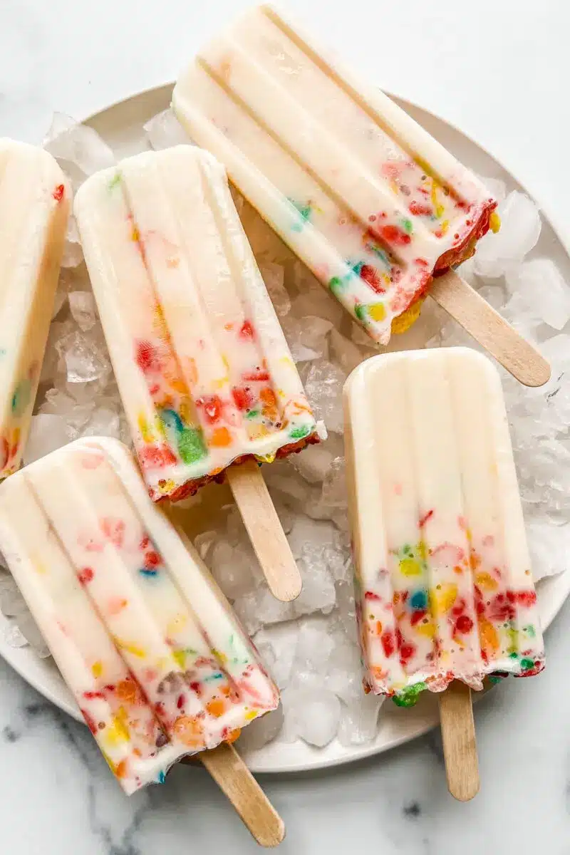 Colorful fruity cereal popsicles over ice on a white plate.