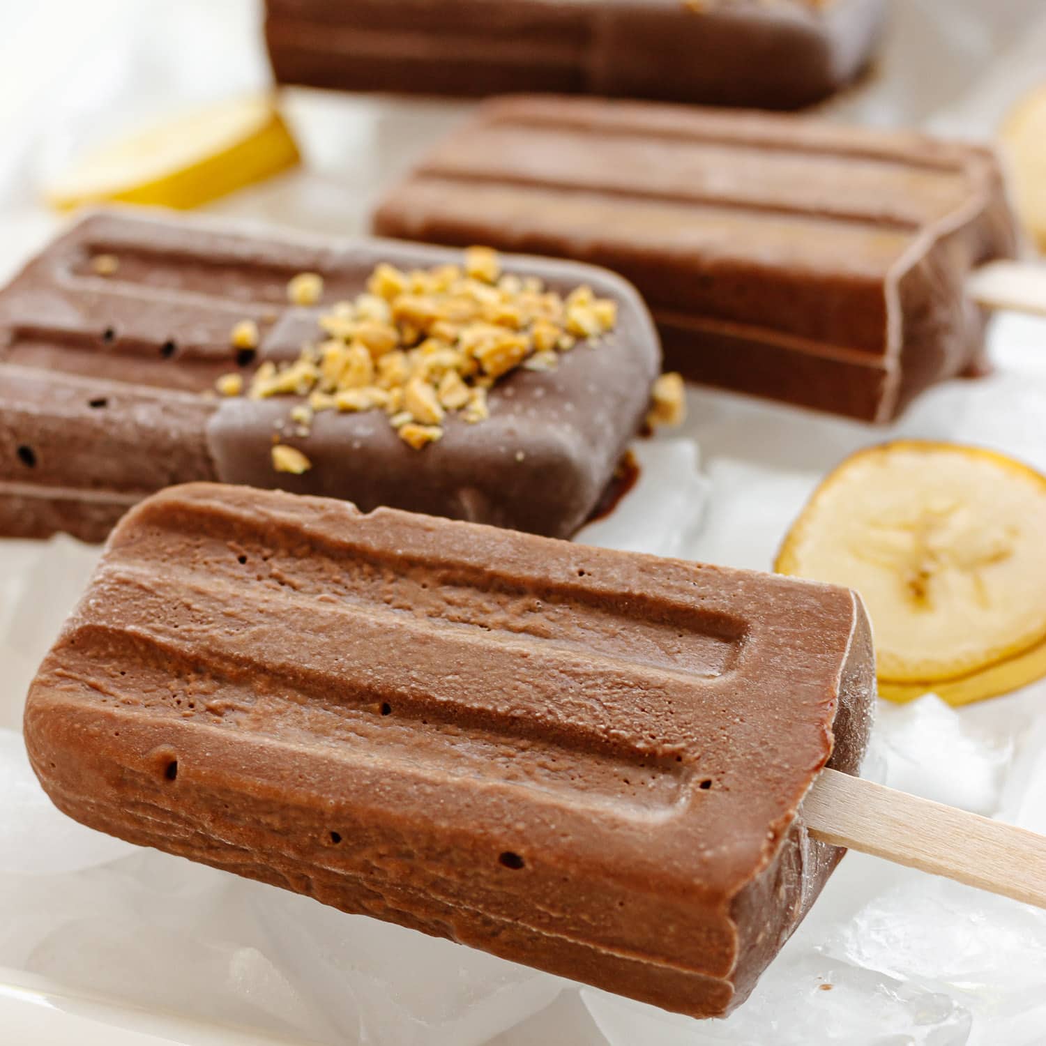 Chocolate banana popsicles over ice with slices of banana.