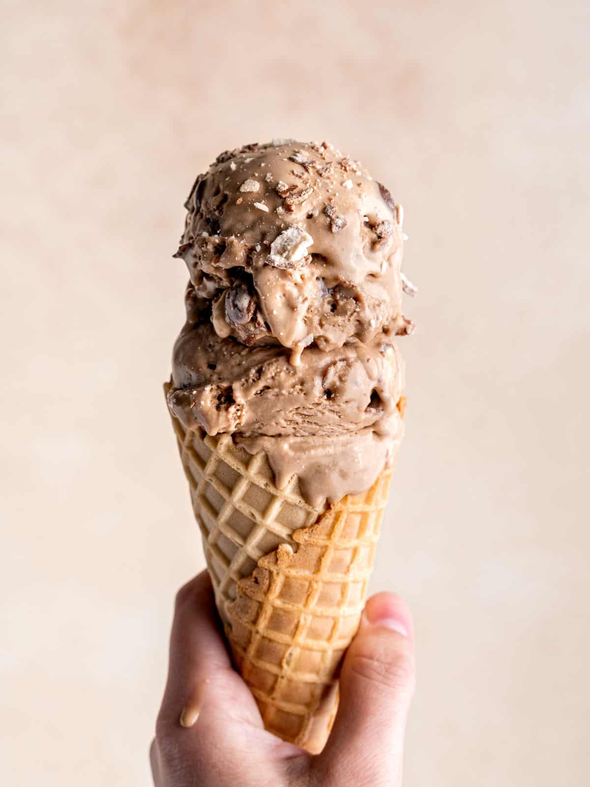 Hand holding a waffle cone with scoops of malted chocolate ice cream.