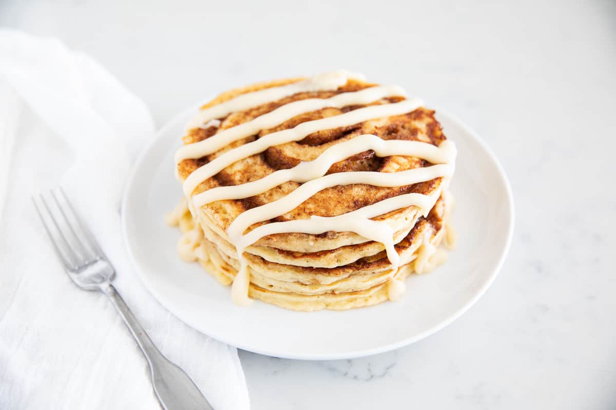 Stack of cinnamon roll pancakes on a white plate.