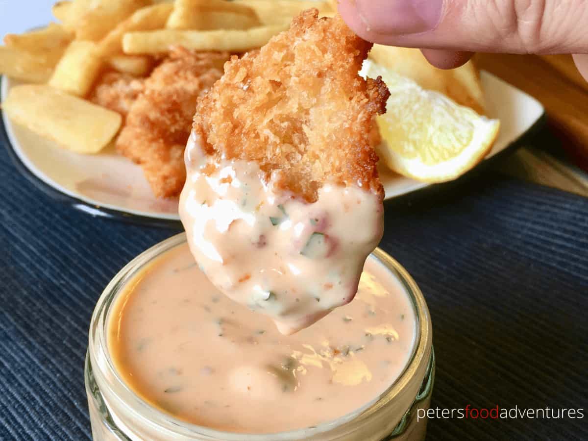 Hand dipping crispy shrimp into bowl full of creamy sweet chili sauce.