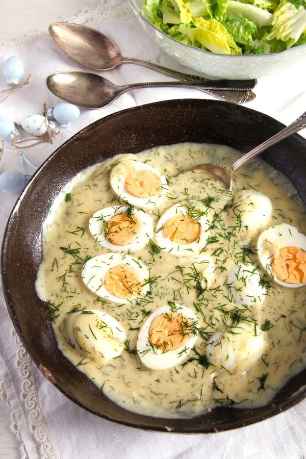 Hard boiled eggs in a skillet with sauce and fresh dill.