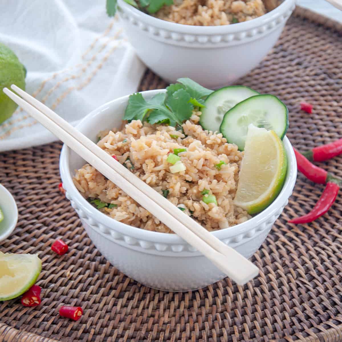 Crab fried rice with cucumbers and lime wedges with chopsticks in a bowl.