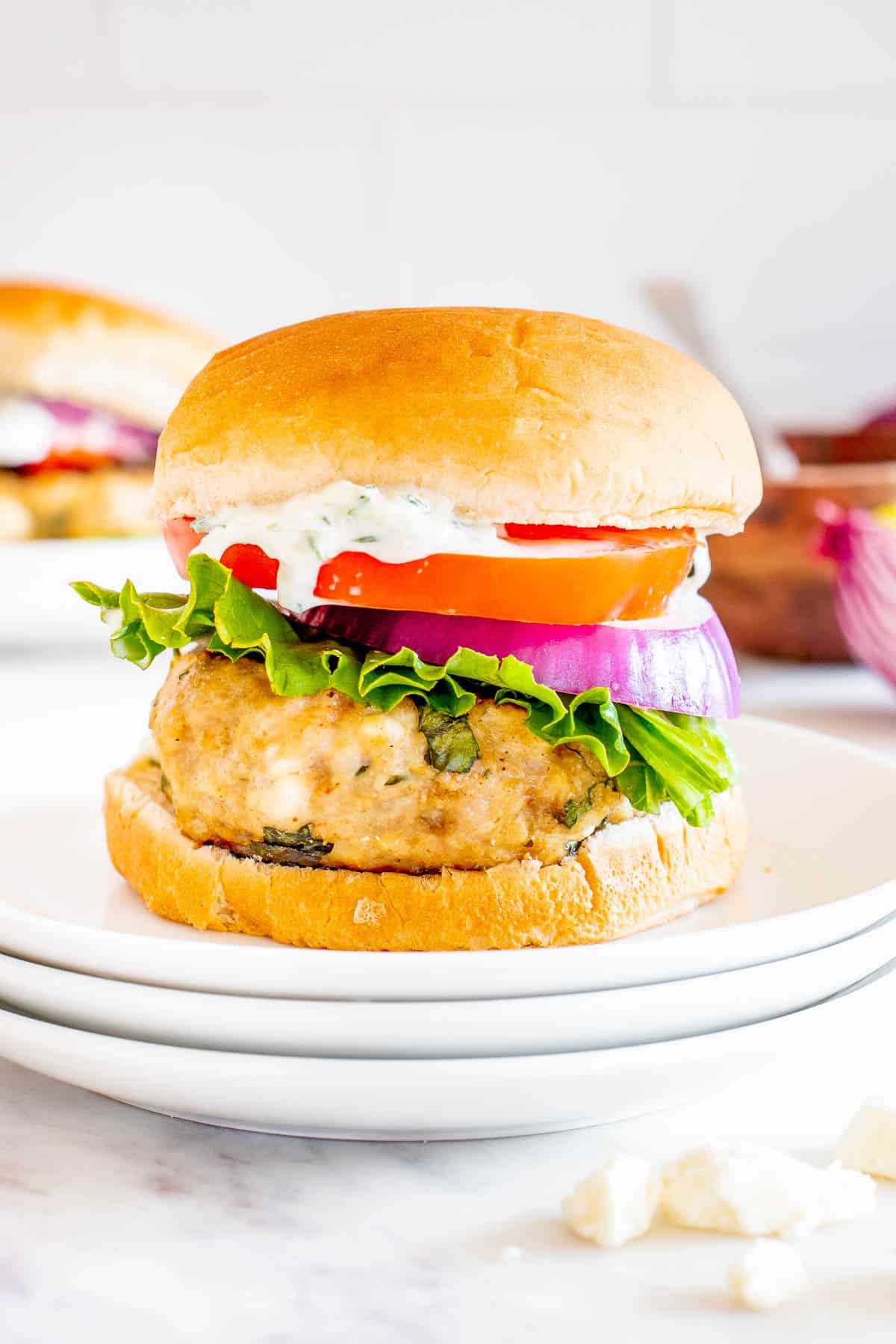 Grilled Greek chicken burger with tomato, onion, lettuce, and tzatziki sauce on a bun.