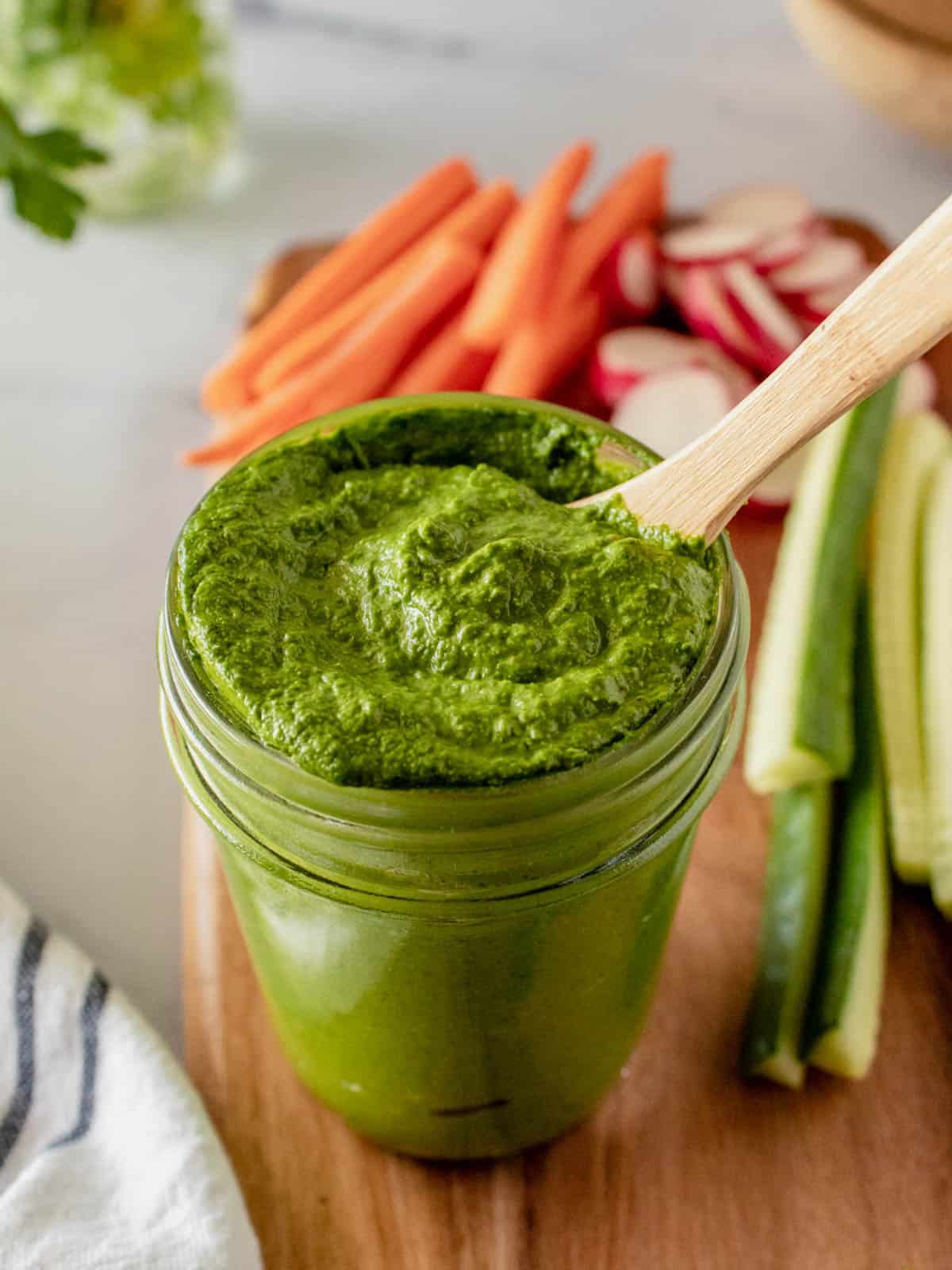 Green tahini sauce in a jar with wooden spoon.