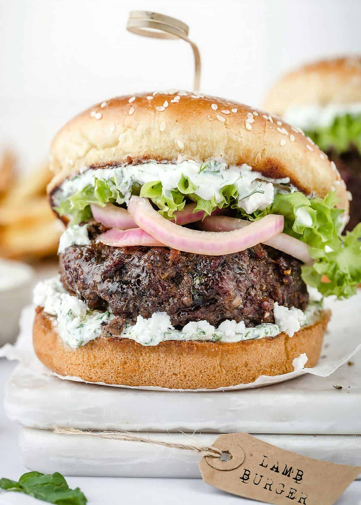 Lamb burger dressed up with pickled red onions, lettuce, and tzatziki sauce on a bun.