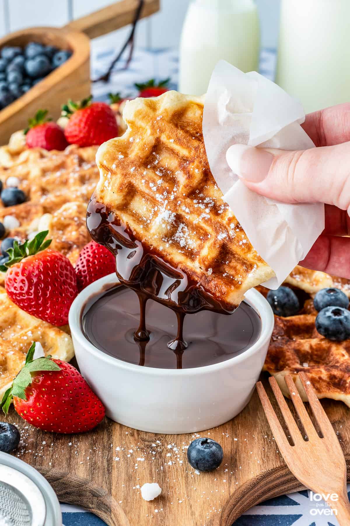 Hand holding a liege waffle dipped in chocolate with berries.