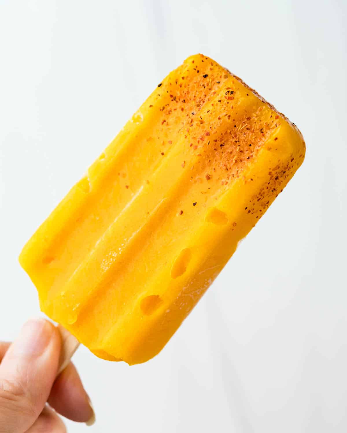 Hand holding mango popsicle with tajin.