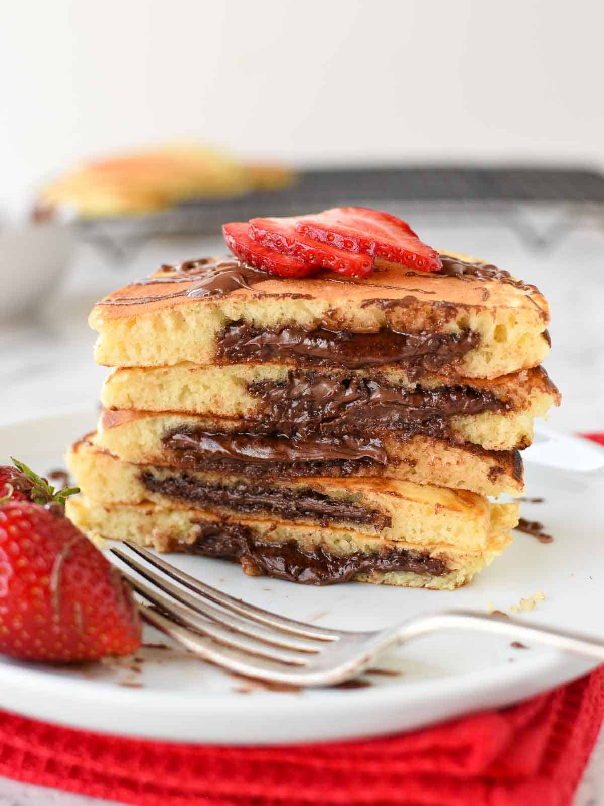 Stack of chocolate filled pancakes with slices of strawberry on a white plate.