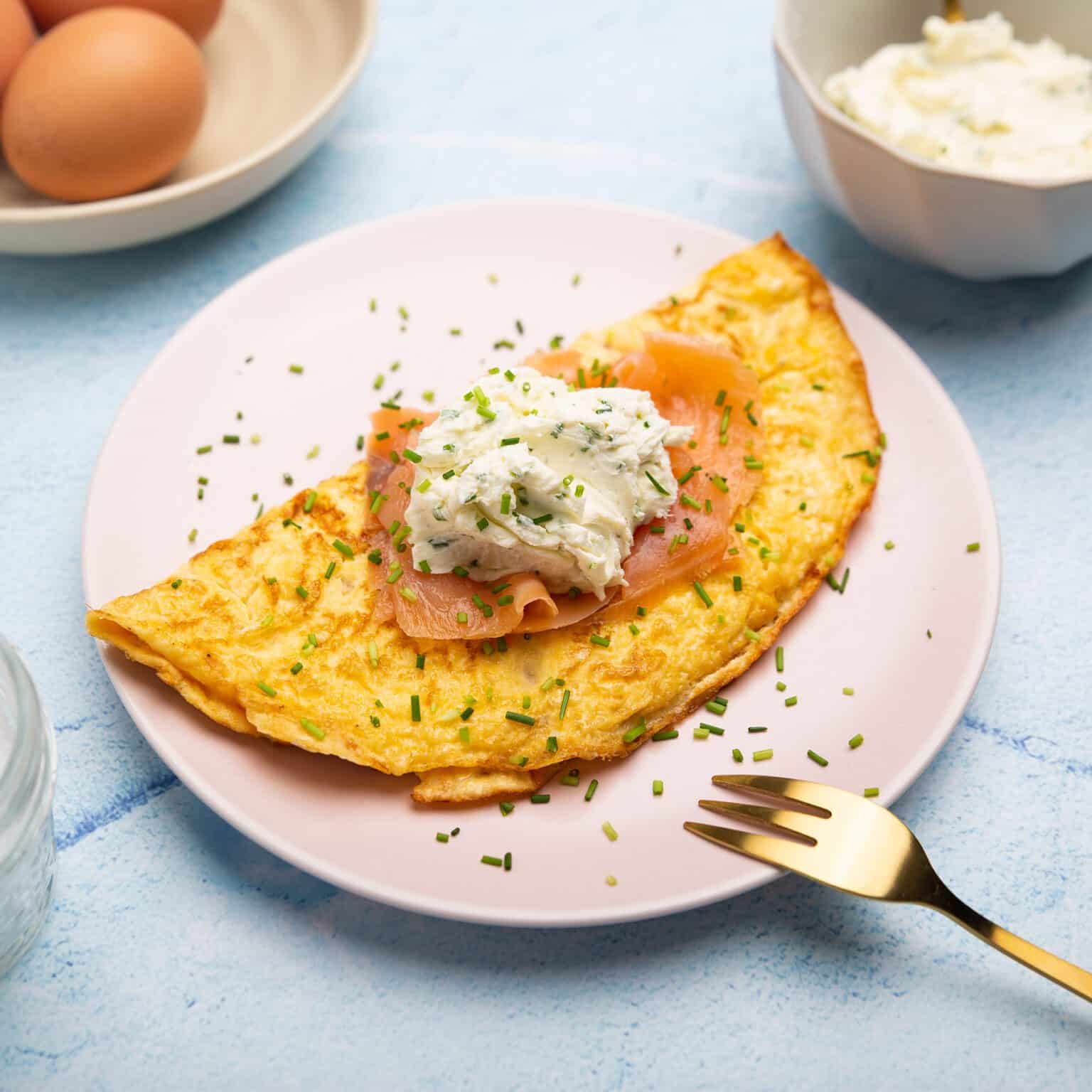 Omelet with smoked salmon and cream cheese on a pink plate with gold fork.